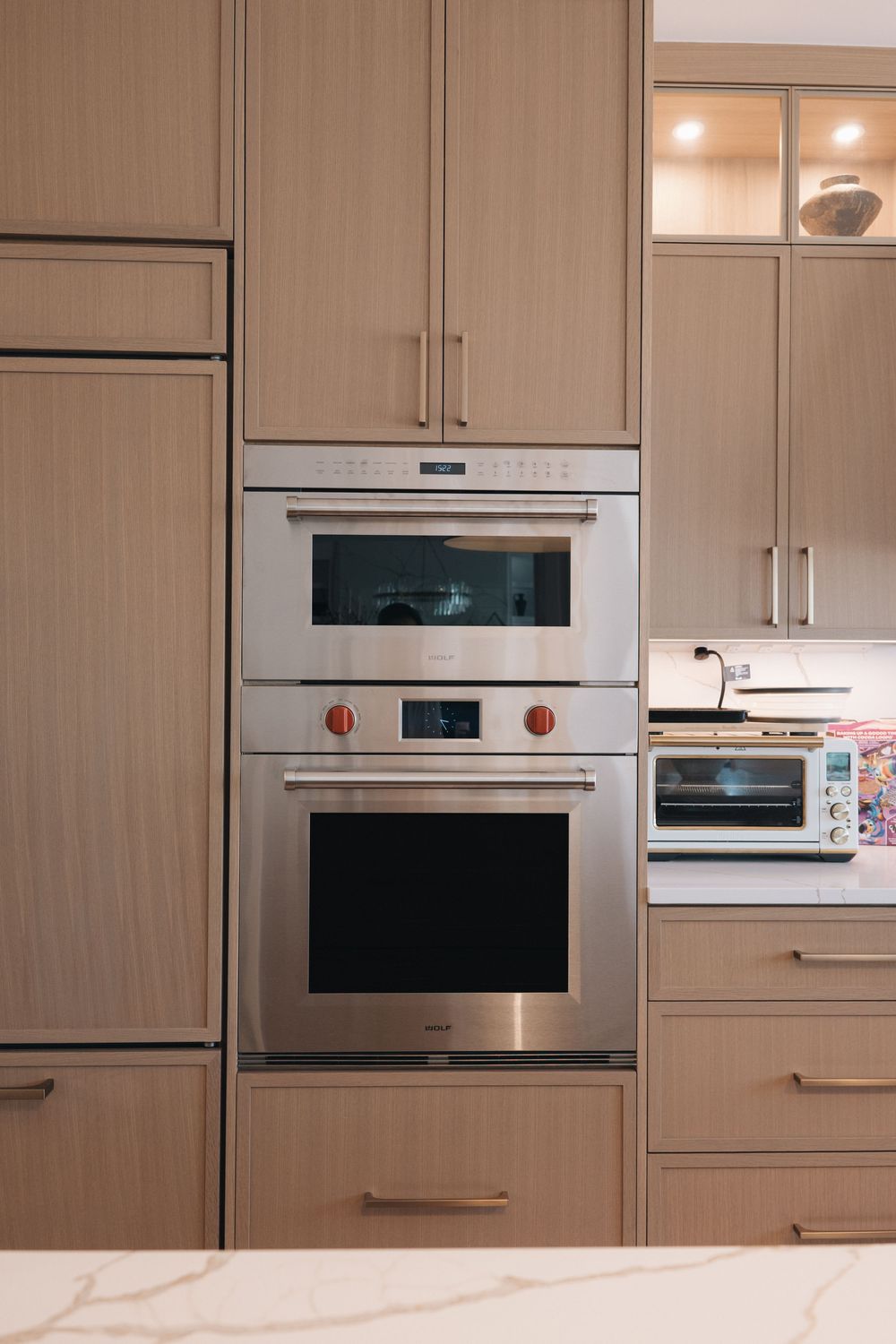 Modern kitchen with Wolf stainless steel double wall oven built into light wood cabinetry with marble countertop.