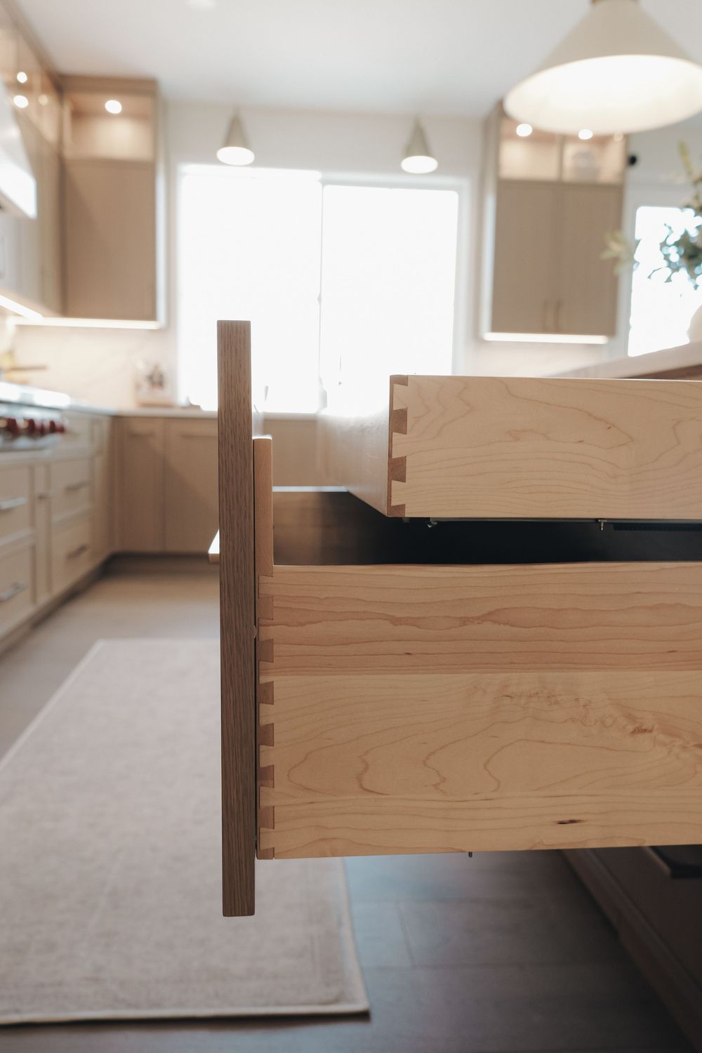Open wooden kitchen drawer with dovetail joints on a light wood cabinet island in a modern kitchen.