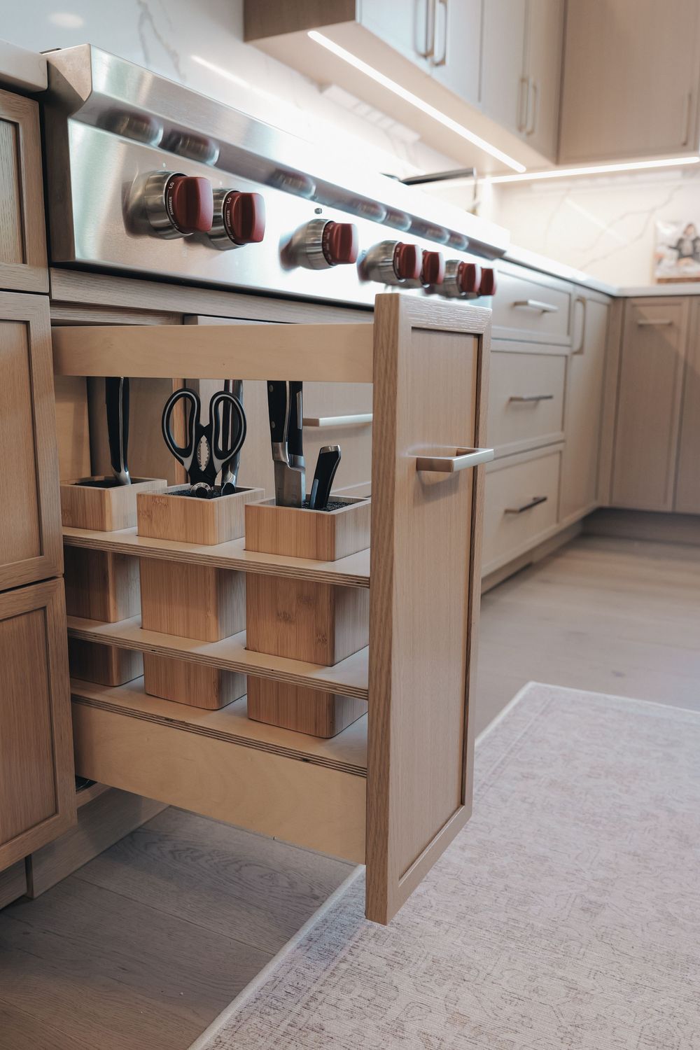 Pull-out kitchen cabinet organizer with wooden knife blocks, scissors, and utensil storage beside a stainless steel range.