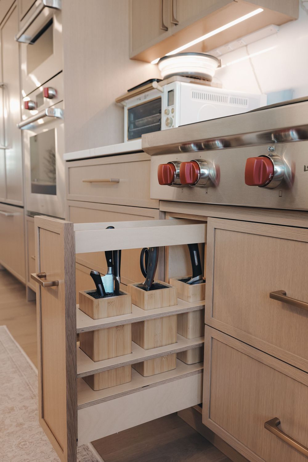 Modern kitchen with pull-out cabinet drawer featuring wooden organizer boxes for utensil storage near a gas stove.