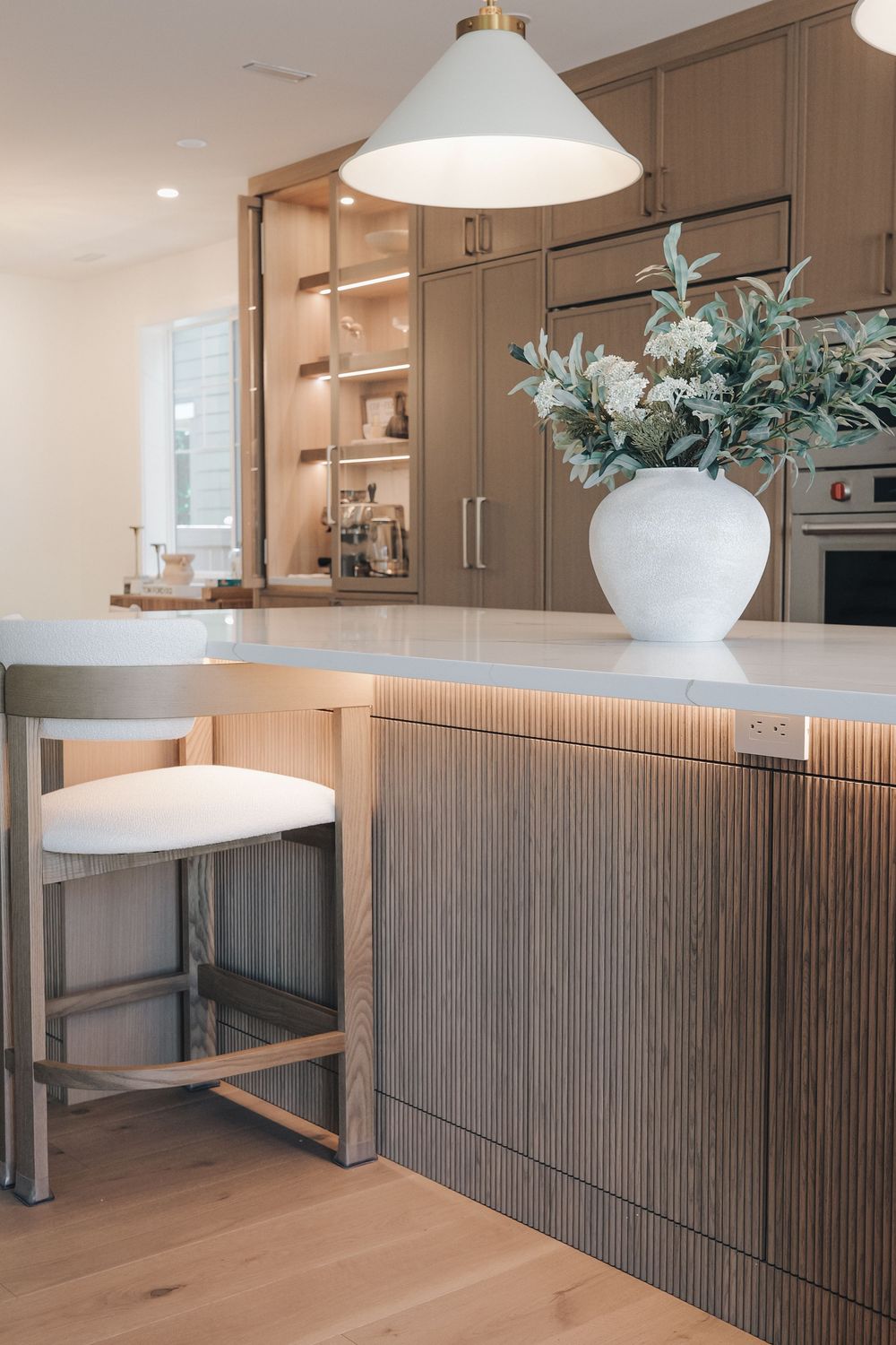 Modern kitchen island with fluted wood panels, white quartz countertop, pendant light, and white vase with greenery.