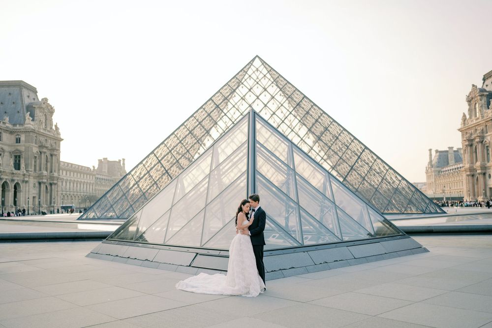 Bride and groom kissing in front of the Louvre Pyramid in Paris at golden hour.