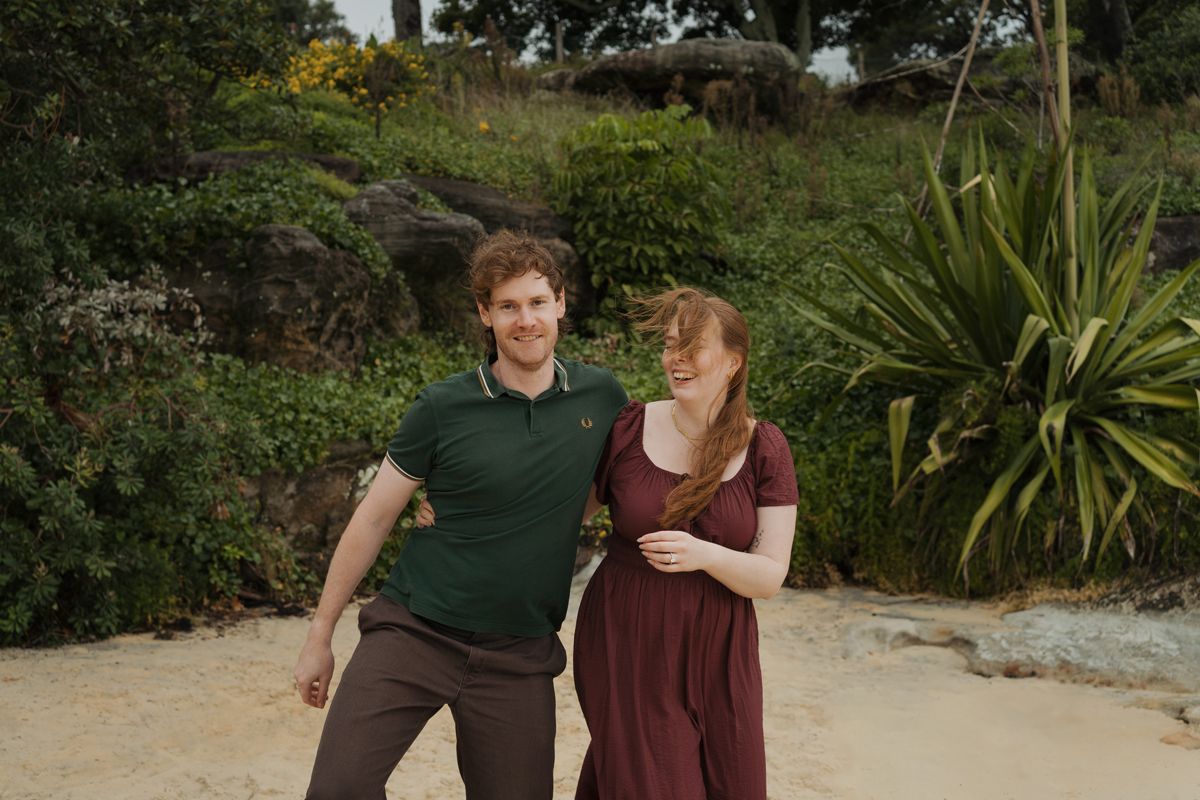 couple poses outdoors on a sandy path surrounded by lush greenery, man in green polo and woman in burgundy dress during proposal photoshoot