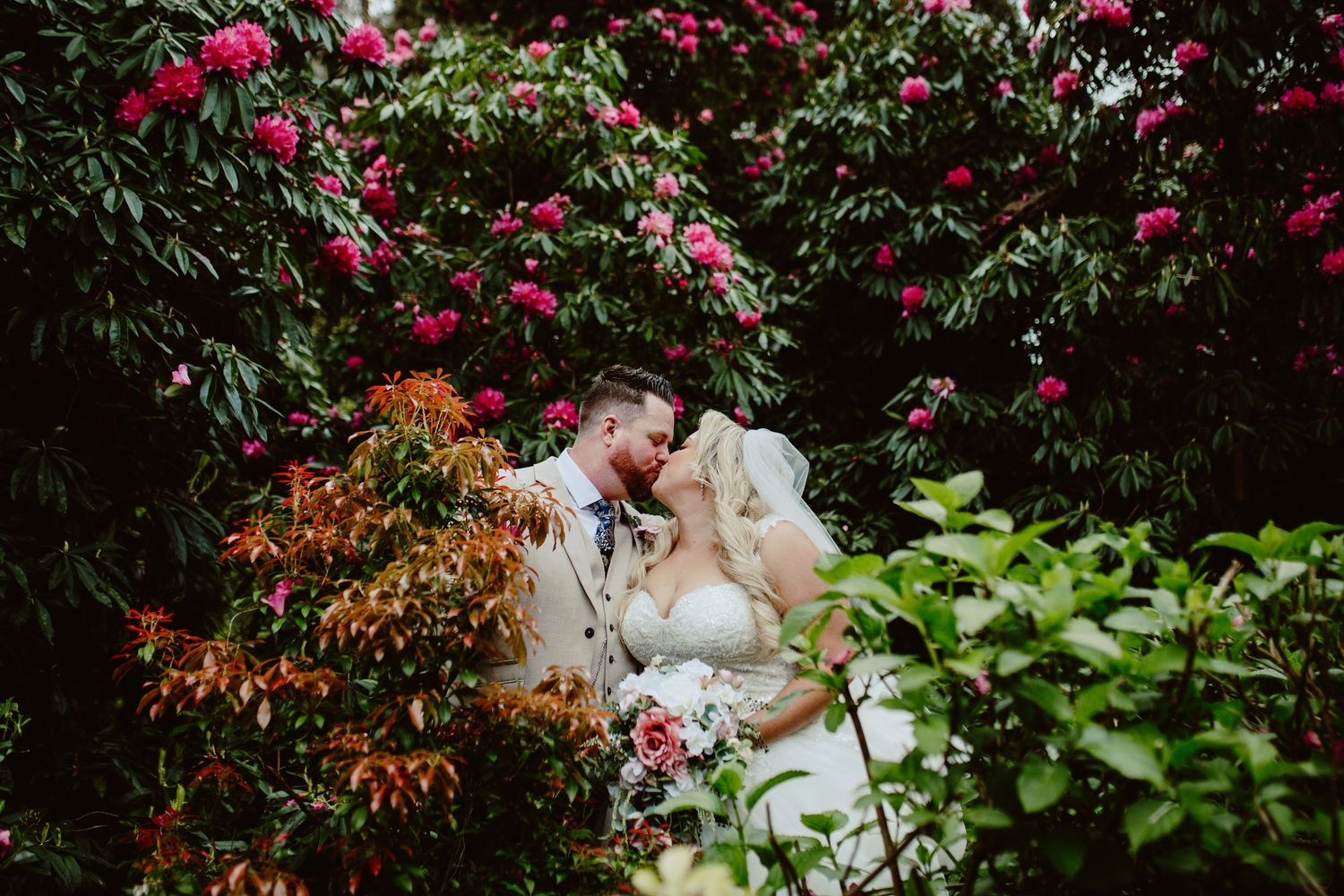 Bride and groom standing before a rustic white barn with red doors on their wedding day.