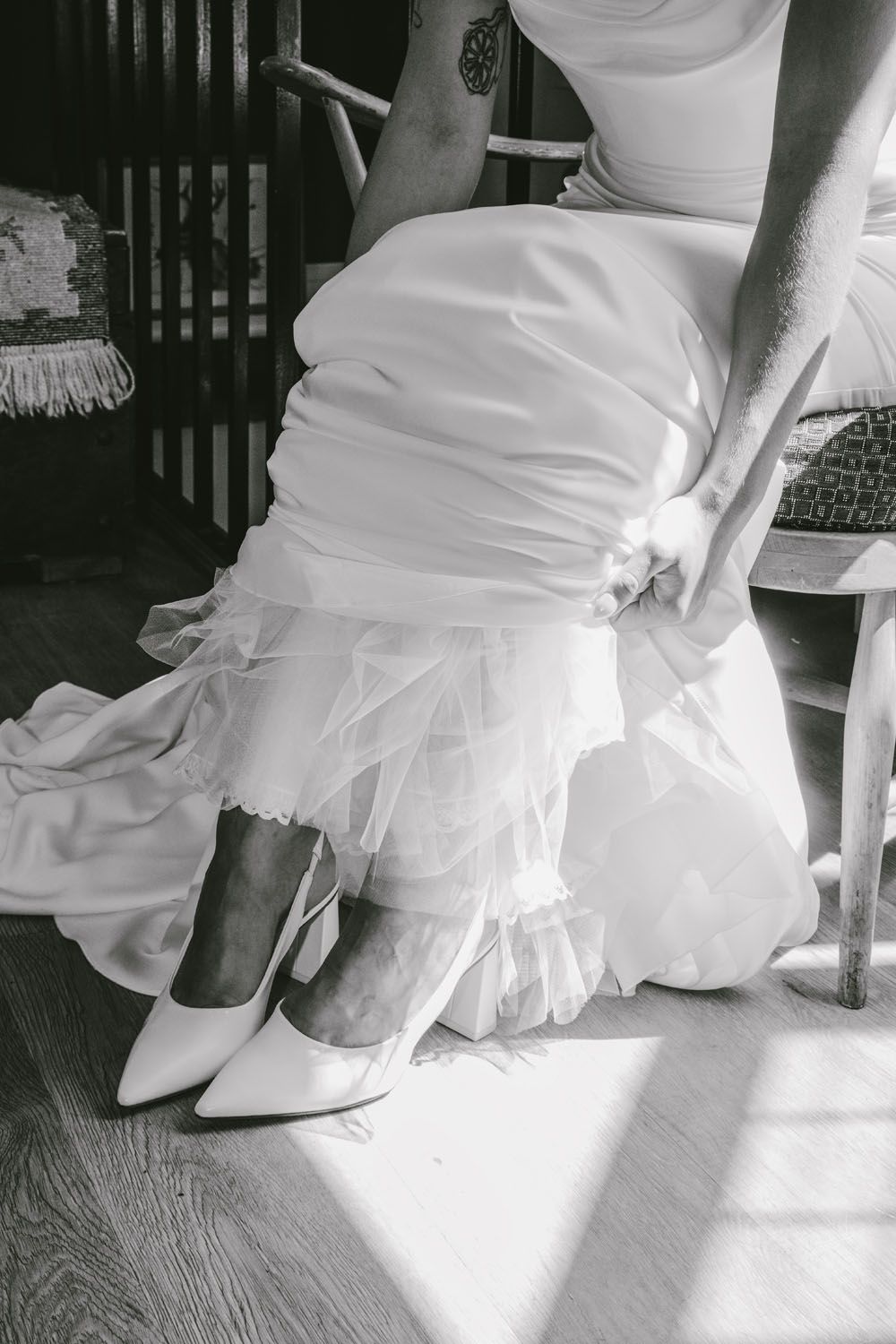 Black and white photo of bride putting on white pointed heels with tulle wedding dress detail.