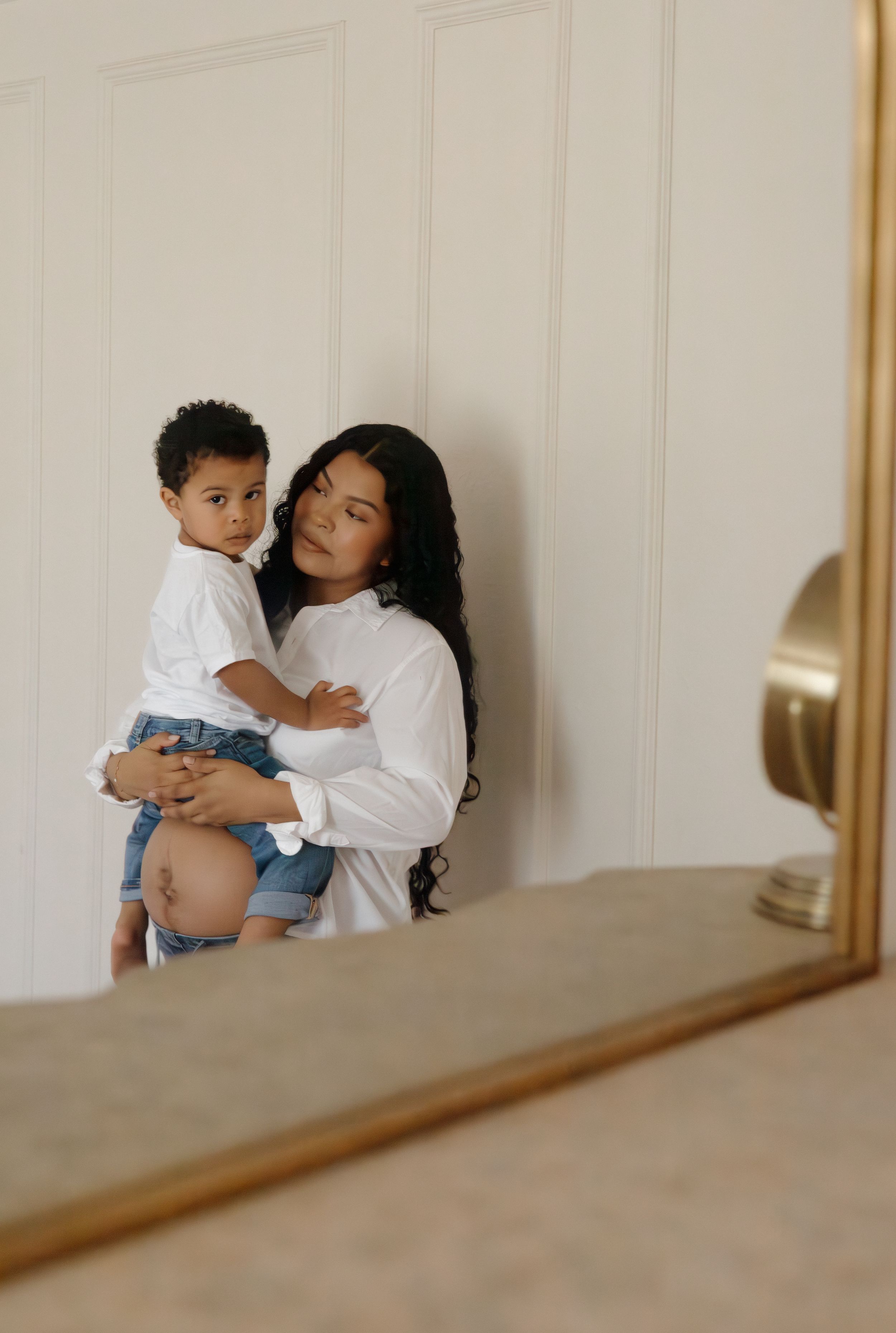 A woman with long dark hair holds a toddler in a white shirt against a white paneled door.