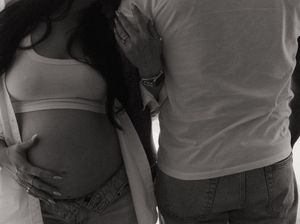 Black and white photo of a couple standing close together, with the woman cradling her pregnant belly.