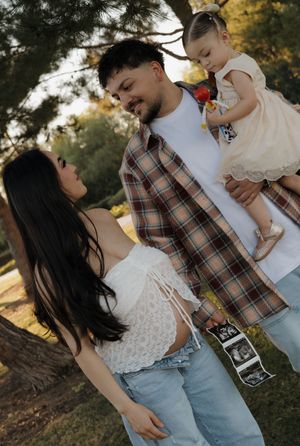 Smiling dad holds toddler on his arm while pregnant mom displays ultrasound photos during family maternity session.