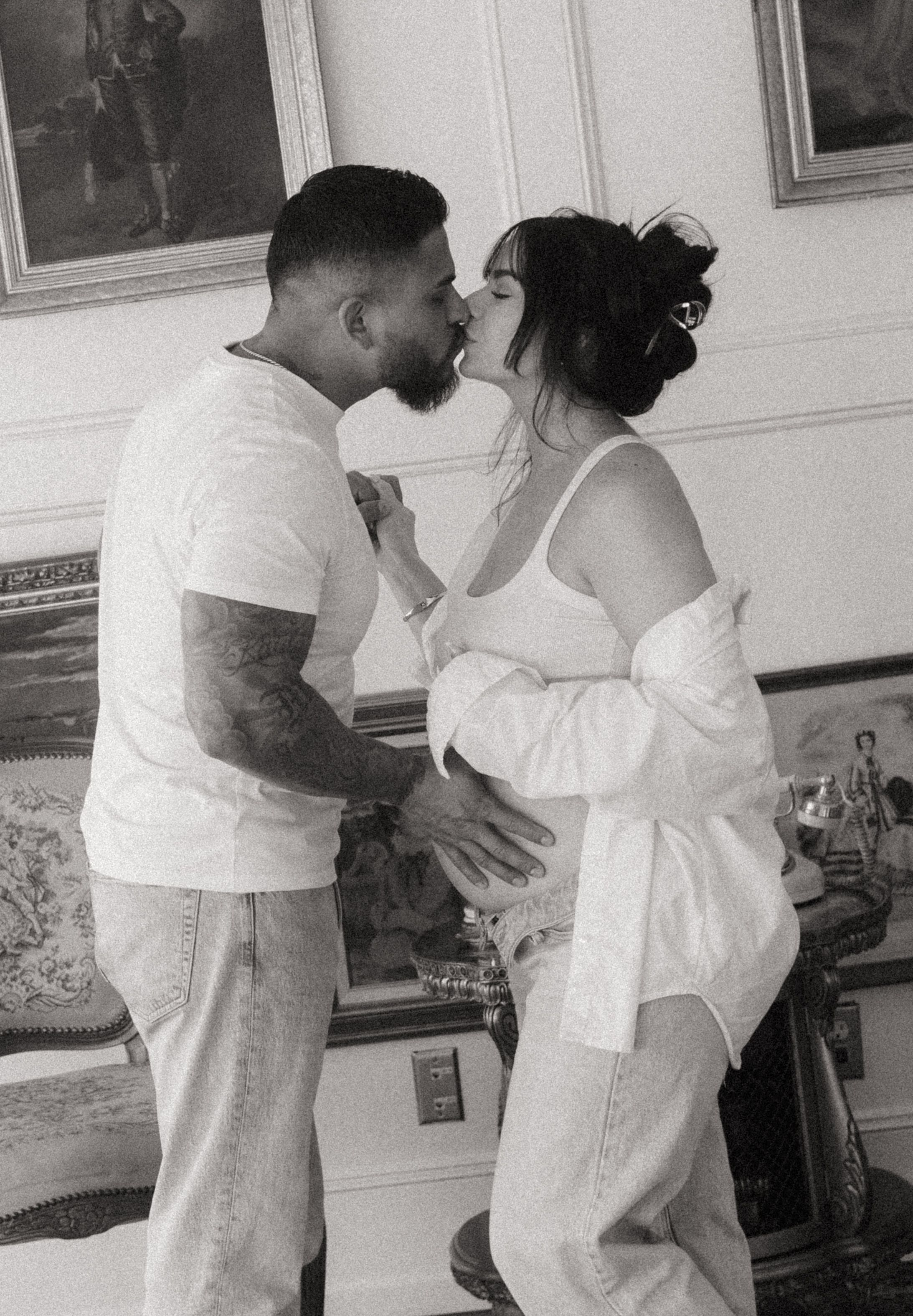 A couple shares a tender kiss during a black and white maternity photo shoot indoors.