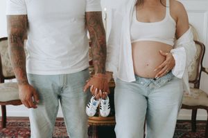 A tattooed man and pregnant woman hold tiny baby shoes together during a maternity shoot.