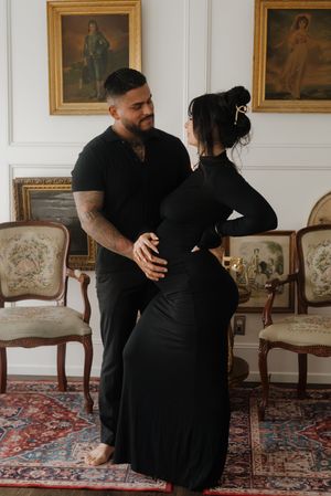 A couple poses together in matching black outfits during an elegant indoor maternity photo session.