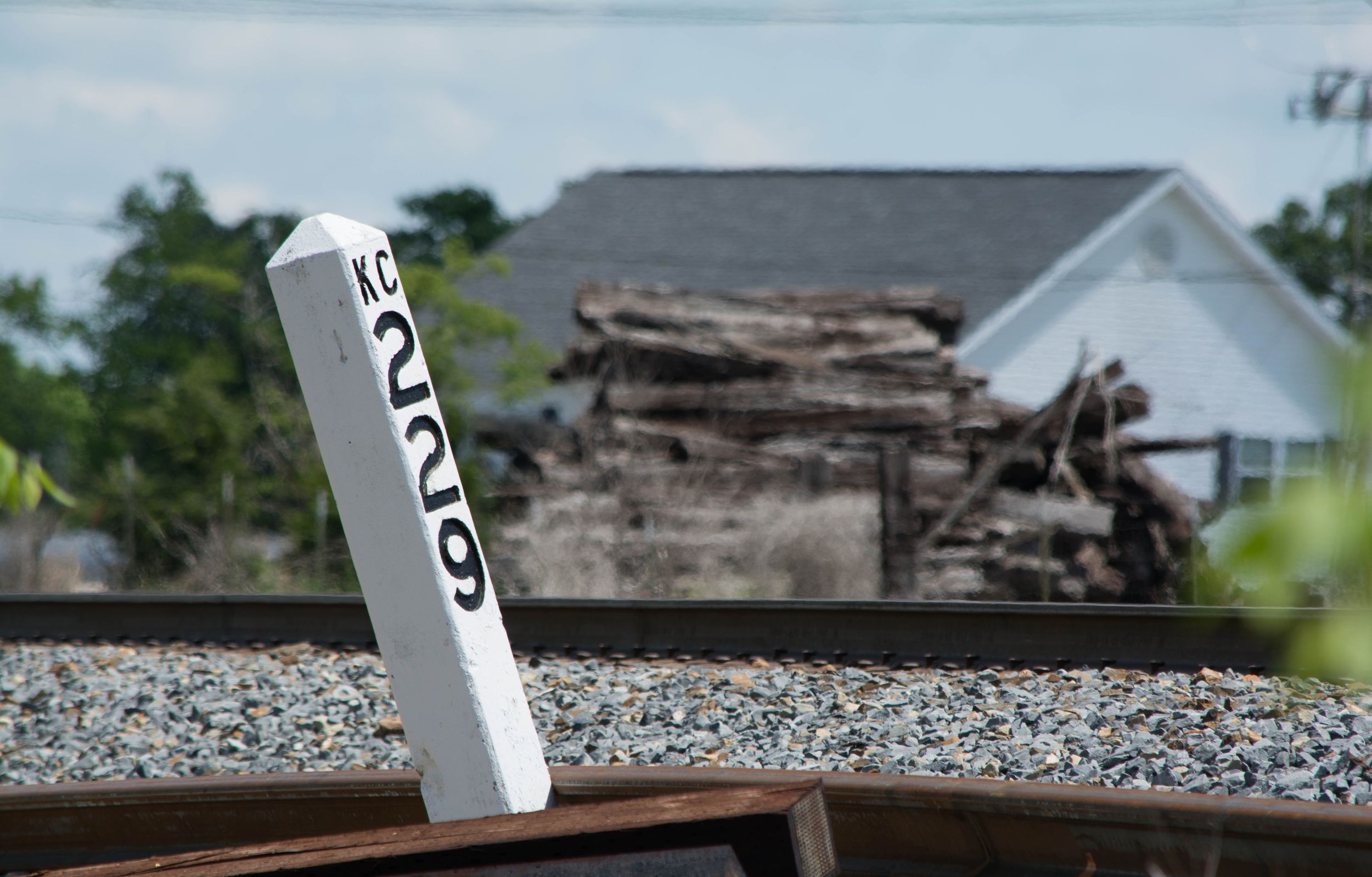 Leaning railroad milepost marker KC 229 with collapsed structure Northwest Arkansas