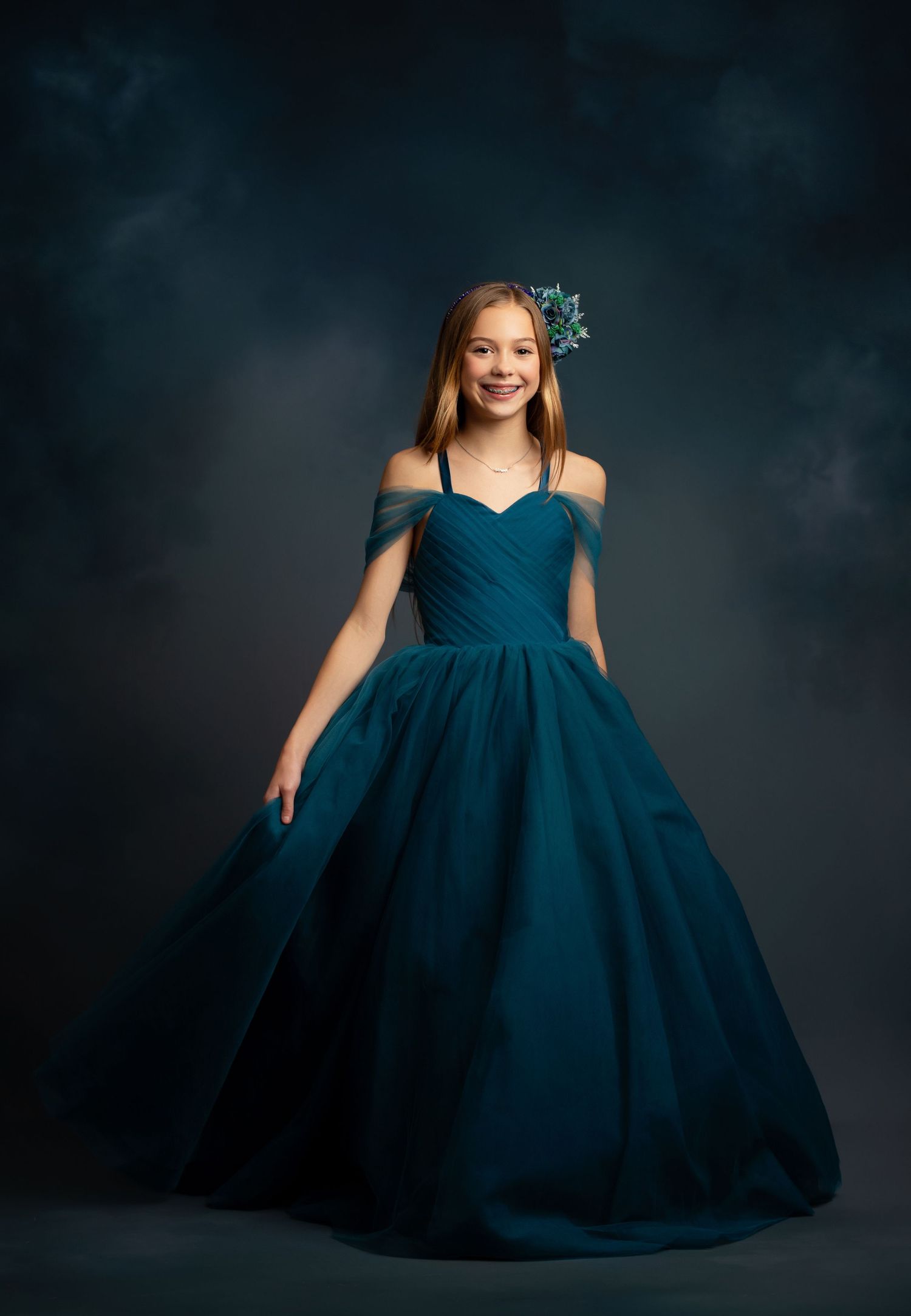 Elegant portrait featuring a ruffled turquoise ball gown against matching blue backdrop.