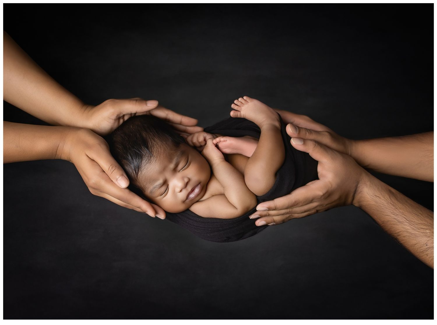 Valerie Kay Photography newborn portrait of baby posed on black cradled in parent's hands.