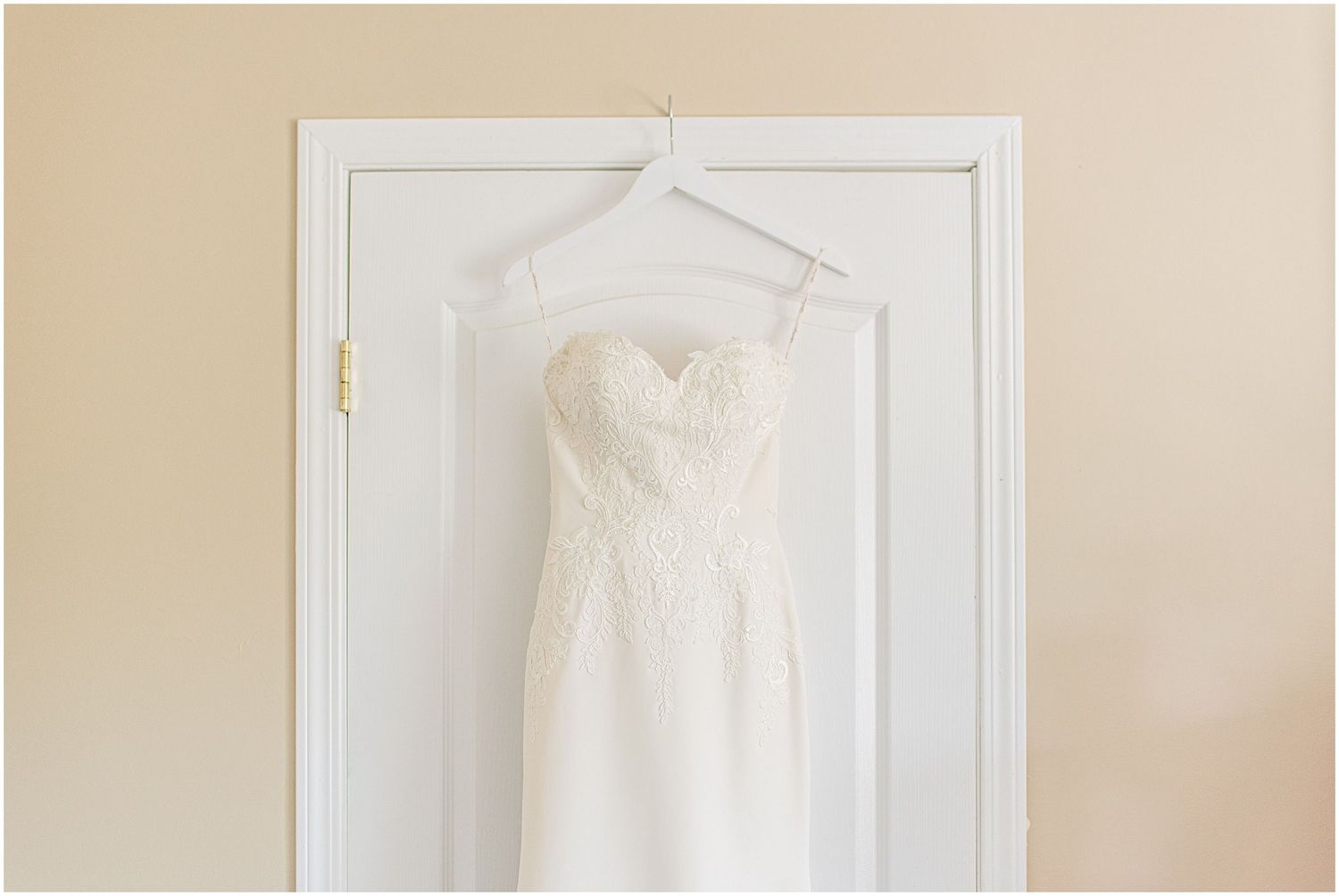 Strapless white lace and satin wedding gown hanging gracefully on a white paneled door.