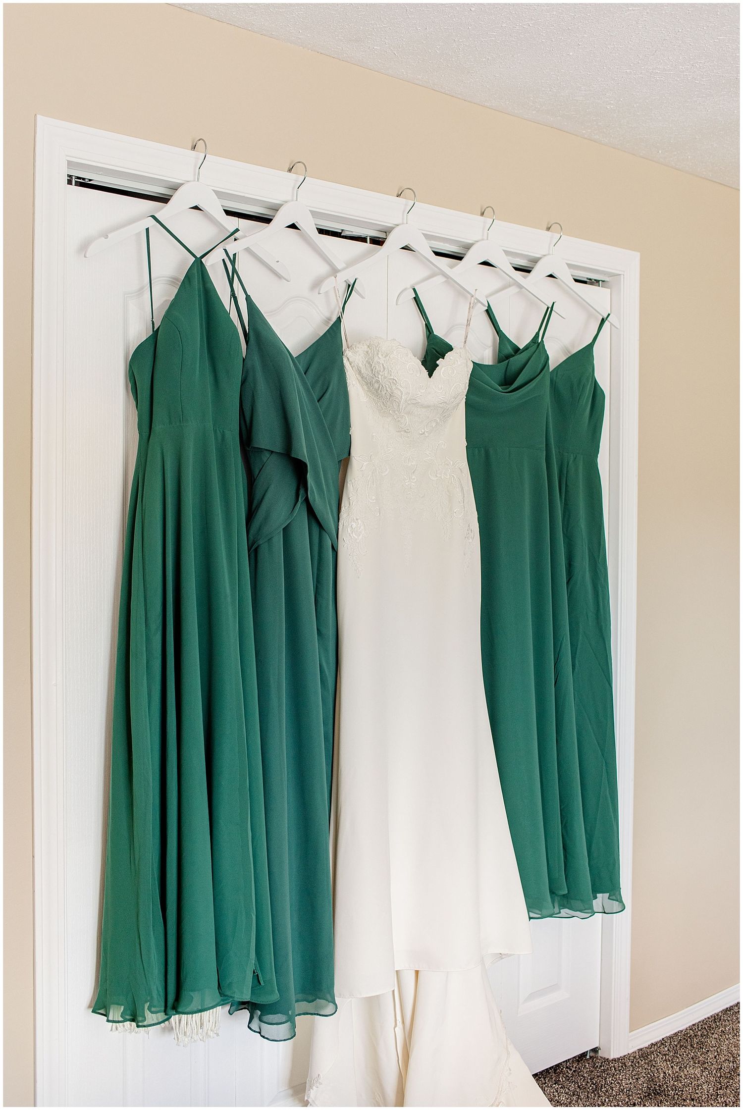 Green bridesmaid dresses and white wedding gown hanging on a door before the ceremony.