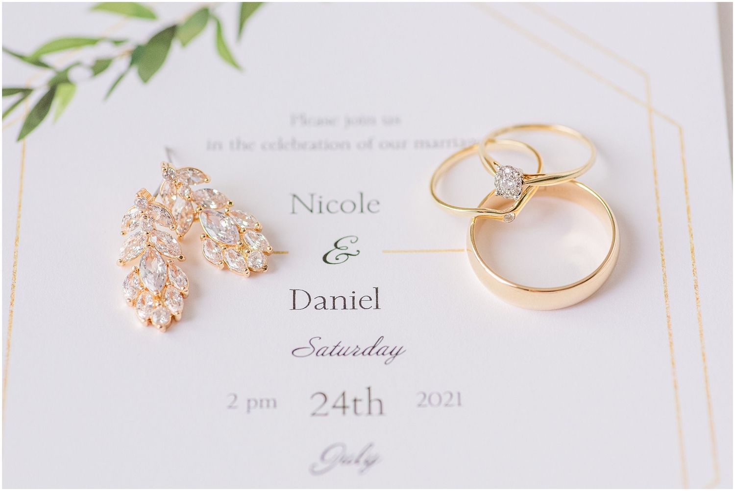 Gold wedding rings and crystal drop earrings displayed on an elegant white wedding invitation for Nicole and Daniel.