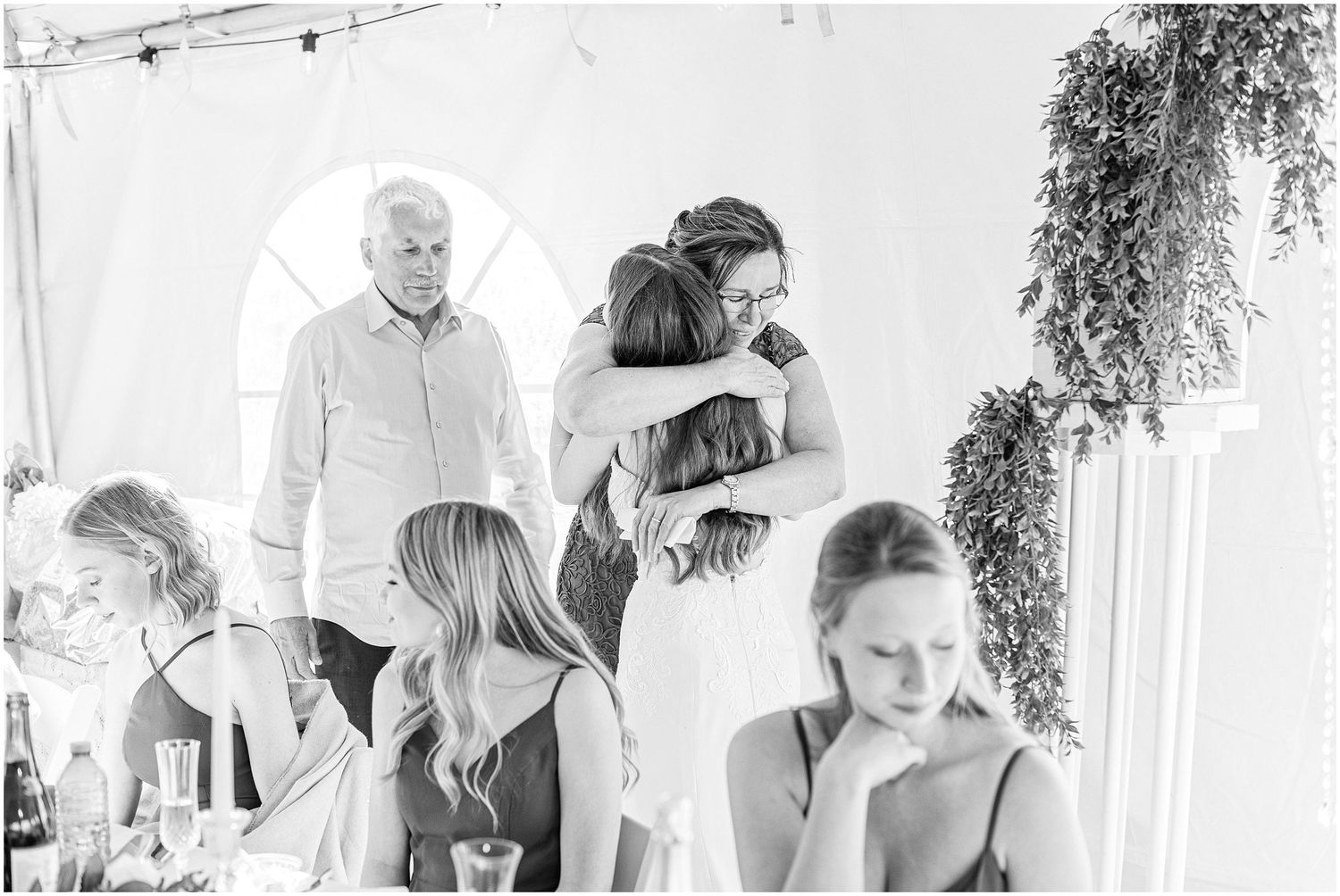 Black and white photo of wedding guests hugging at reception celebration.
