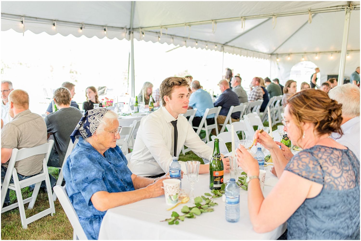 Wedding reception guests seated under a white tent, toasting with champagne glasses at elegantly decorated tables.