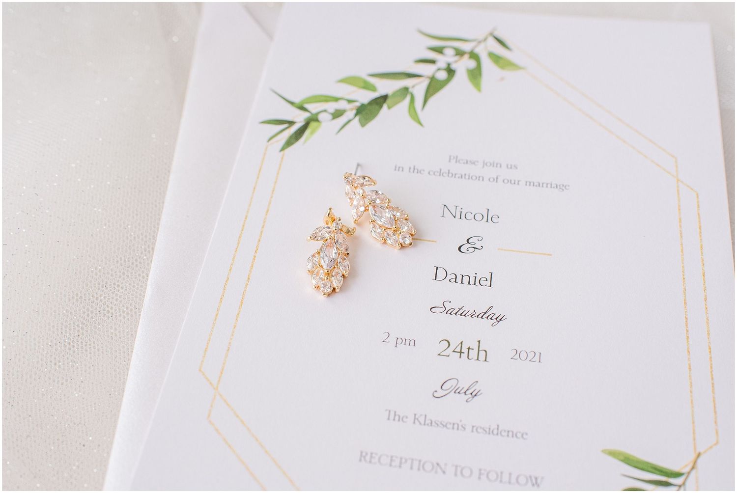Crystal drop earrings resting on a white and gold geometric wedding invitation for Nicole and Daniel's July 2021 wedding.