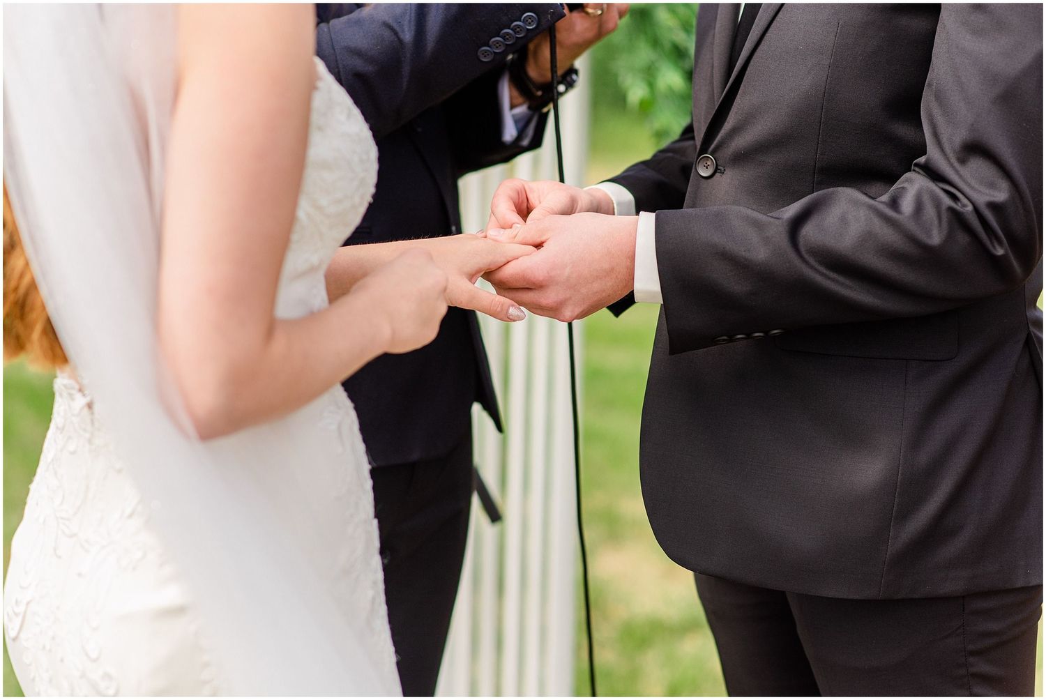 Bride and groom exchanging wedding rings during outdoor ceremony, close-up of hands.