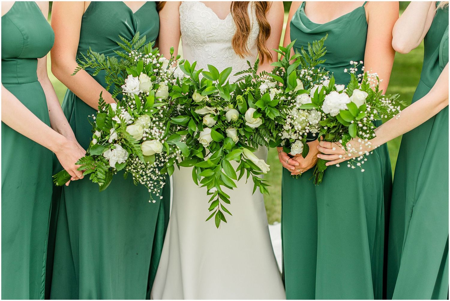 Bride and bridesmaids in emerald green gowns display lush green and white floral bouquets.