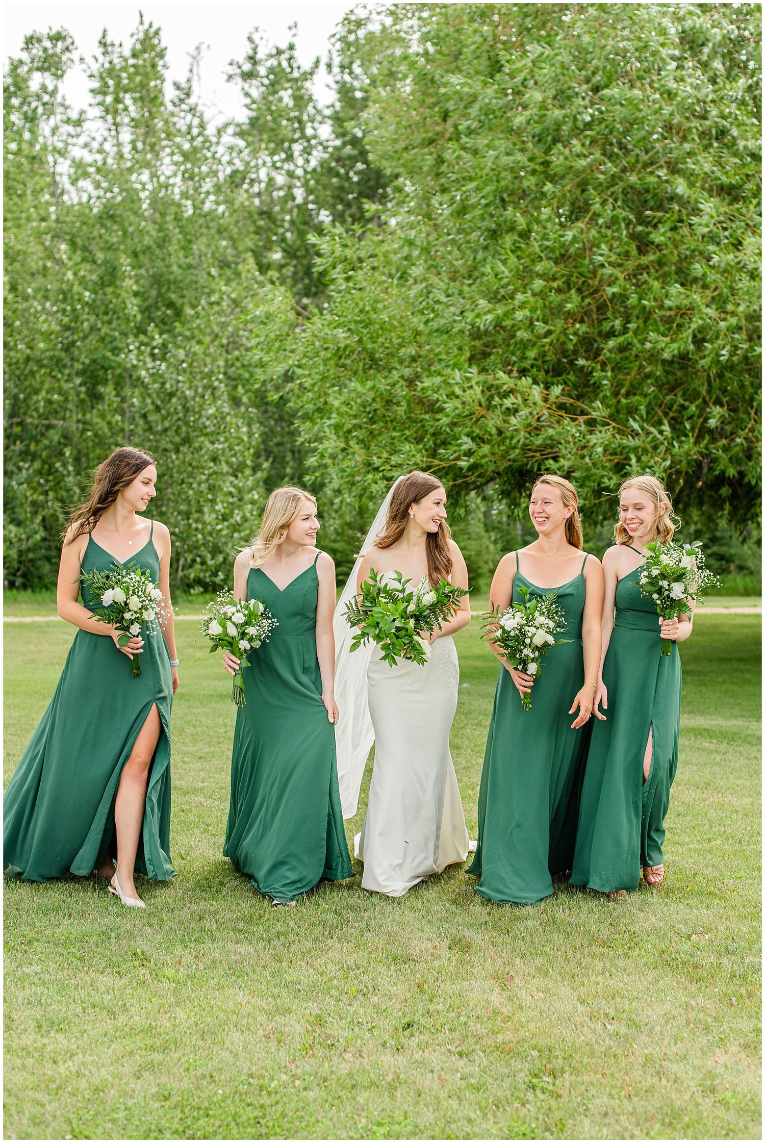 Bride walks with four bridesmaids in emerald green gowns carrying white bouquets.
