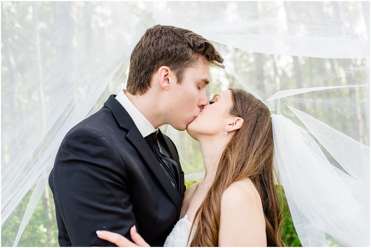Bride and groom share a romantic kiss beneath a flowing white veil on their wedding day.