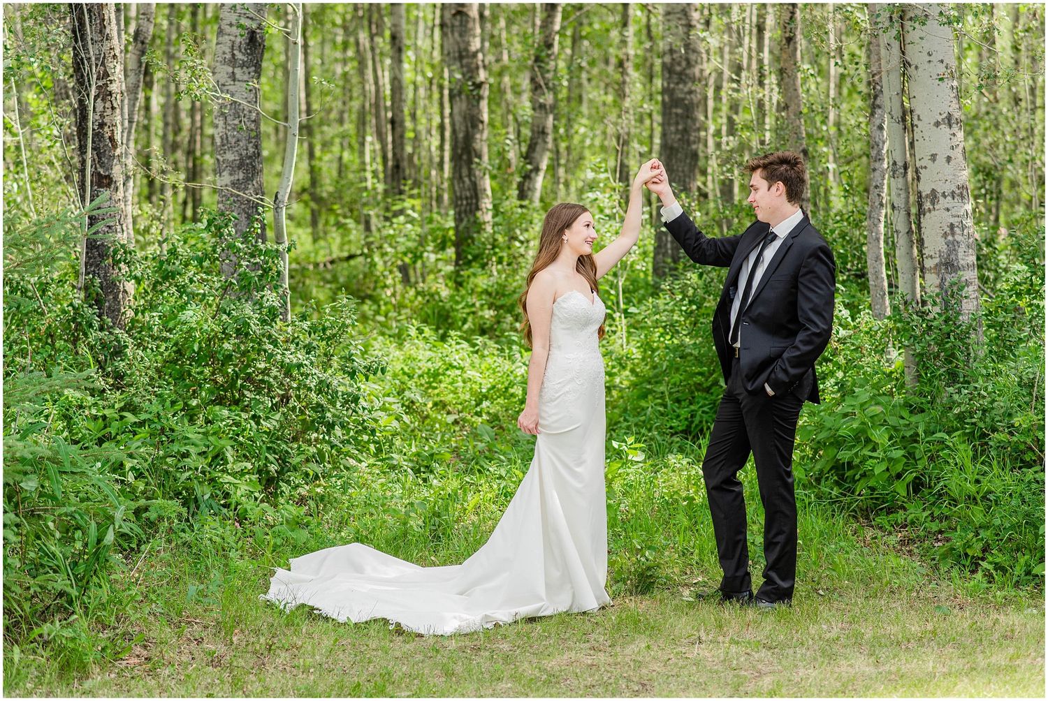 Bride and groom dancing together in a lush green forest clearing during their wedding photo session.