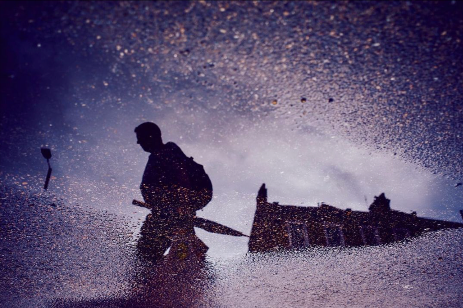 Silhouette of a soldier reflected in a rain-splashed puddle with purple hues and dramatic water droplets.