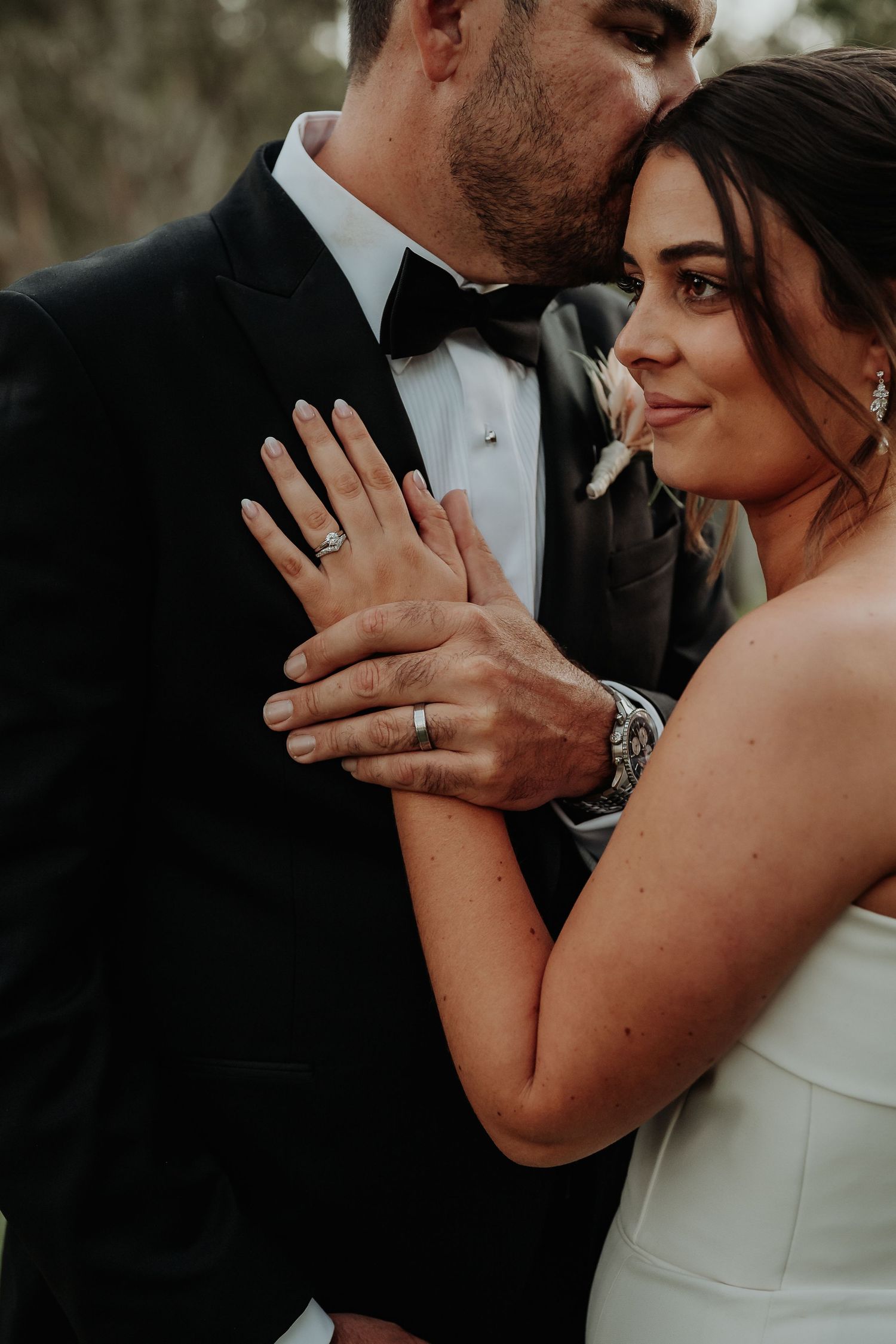 Bride and groom in elegant wedding attire share a tender moment, showcasing their wedding rings in a romantic close-up.