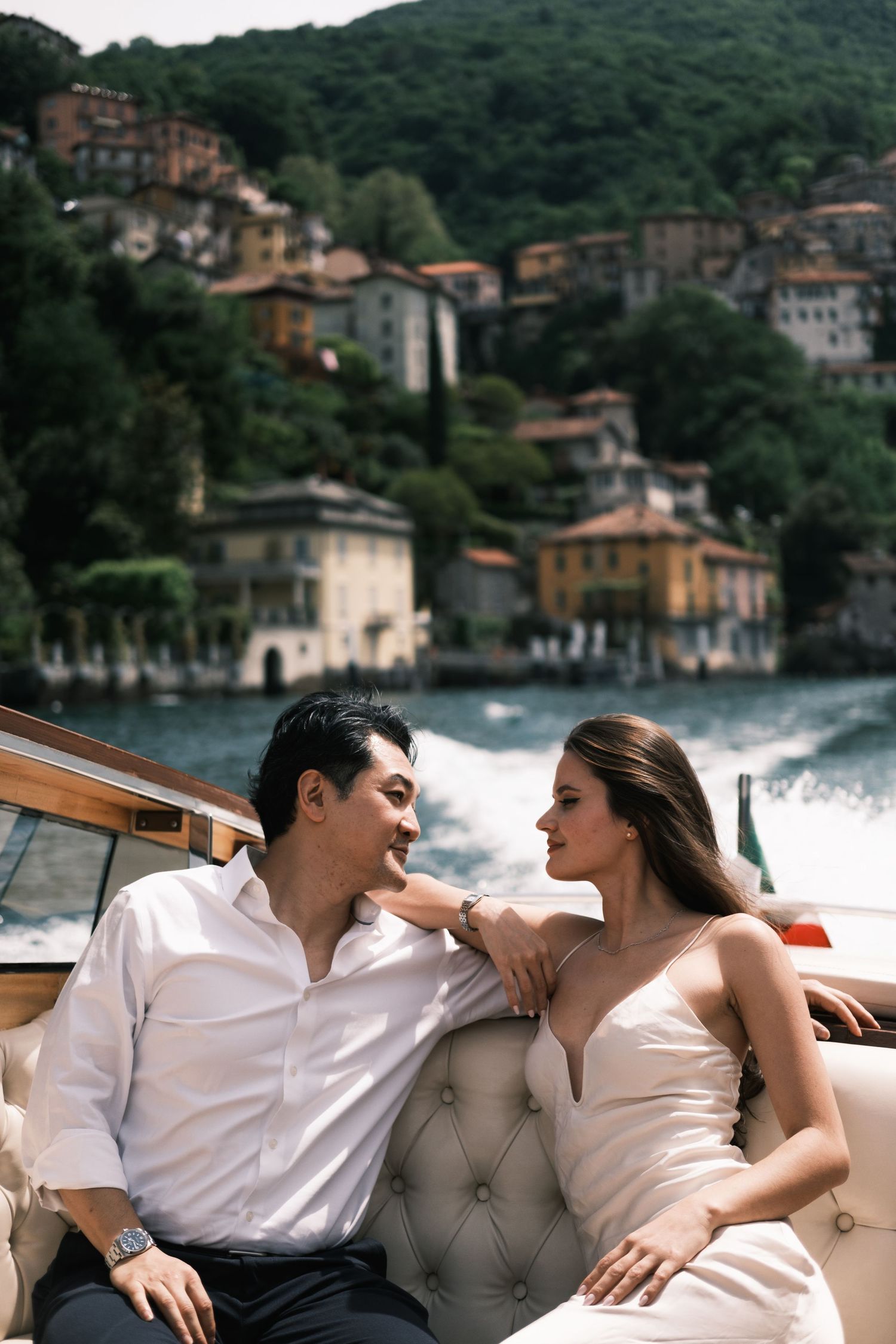 Elegant couple sitting on a luxury boat with Italian lakeside village in background on Lake Como.