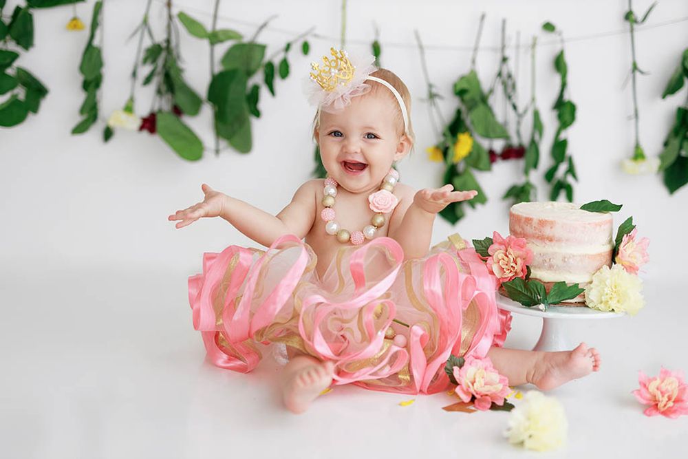 Happy baby girl in pink tutu dress laughing near birthday cake smash with flowers by professional Winchester baby photographer.