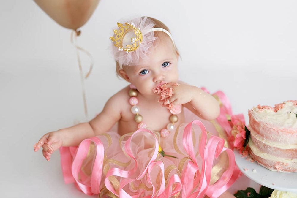 Professional Winchester baby photographer photo of baby girl in pink tutu eating cake during first birthday smash cake photo session.