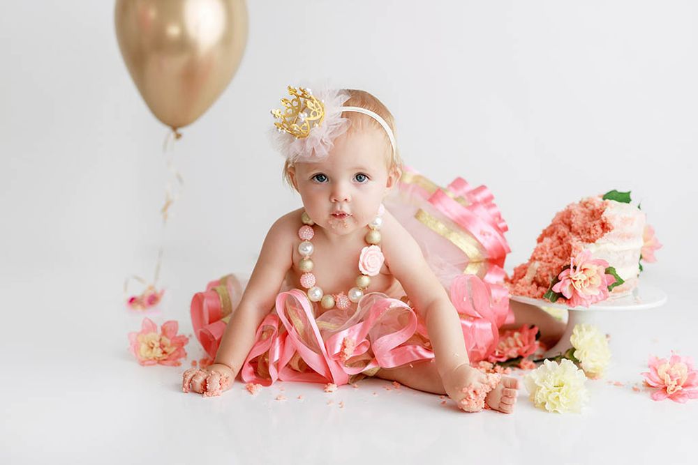 Baby girl in pink tutu and pearl necklace celebrates first birthday with cake and gold balloon by Winchester baby photographer.