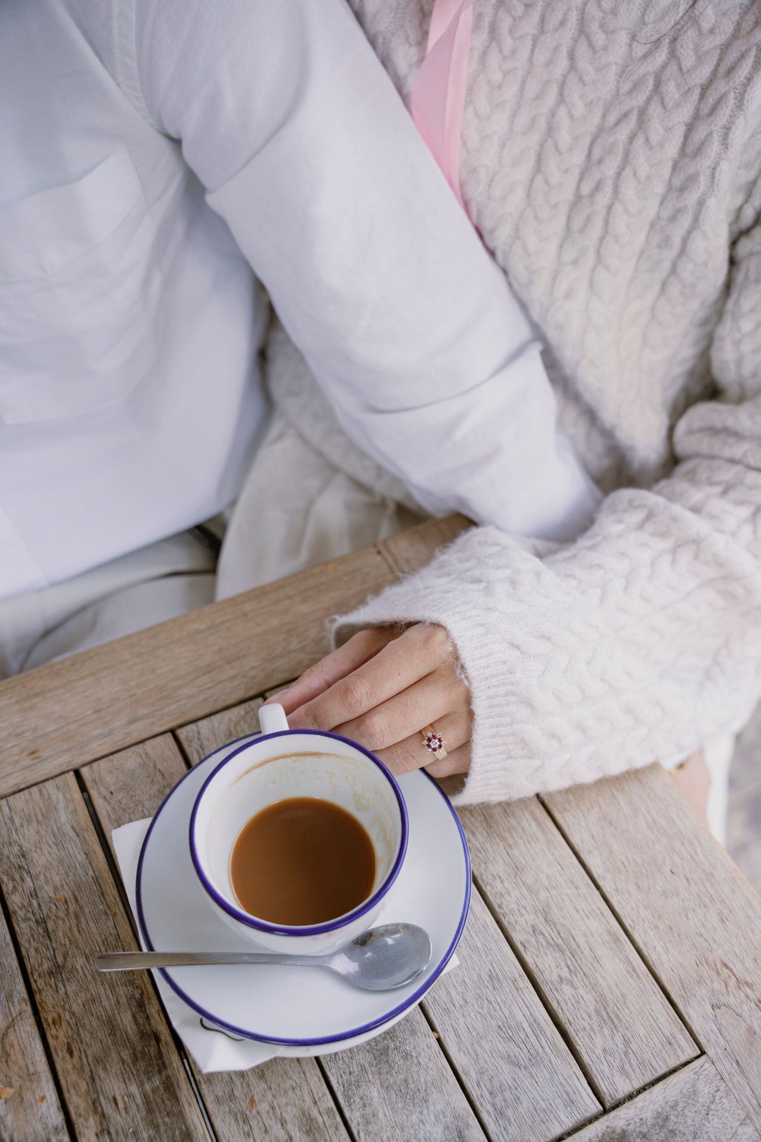 Close-up of a couple at a cafe table with a coffee cup and a ring on her finger.