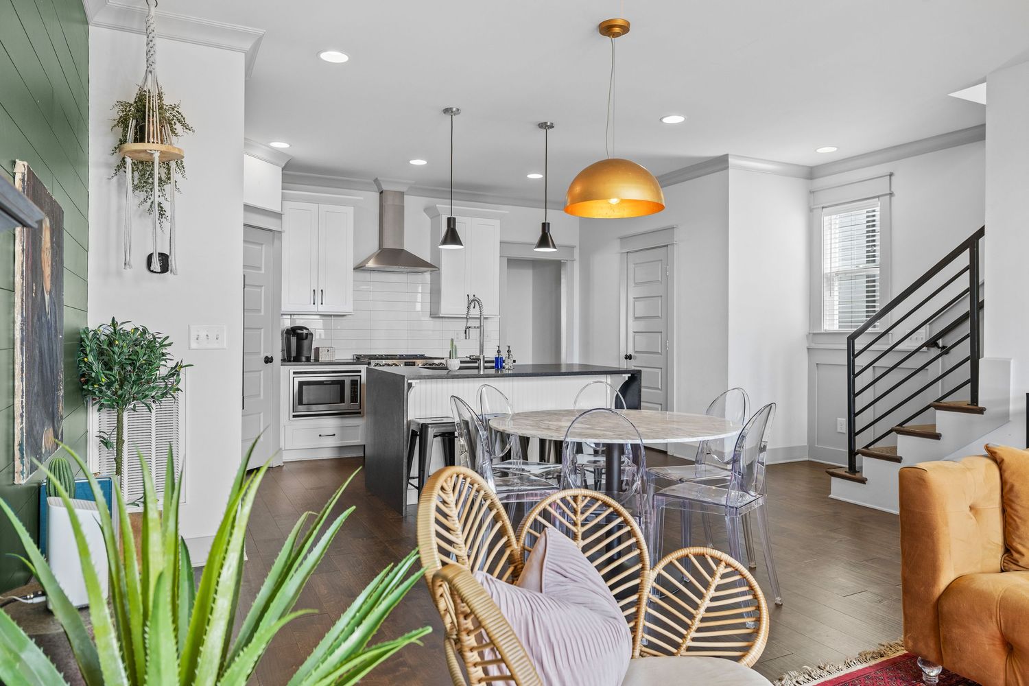 Modern open-concept kitchen with gray pendant lights, brick walls, dark island with bar stools, and teal velvet sofa.