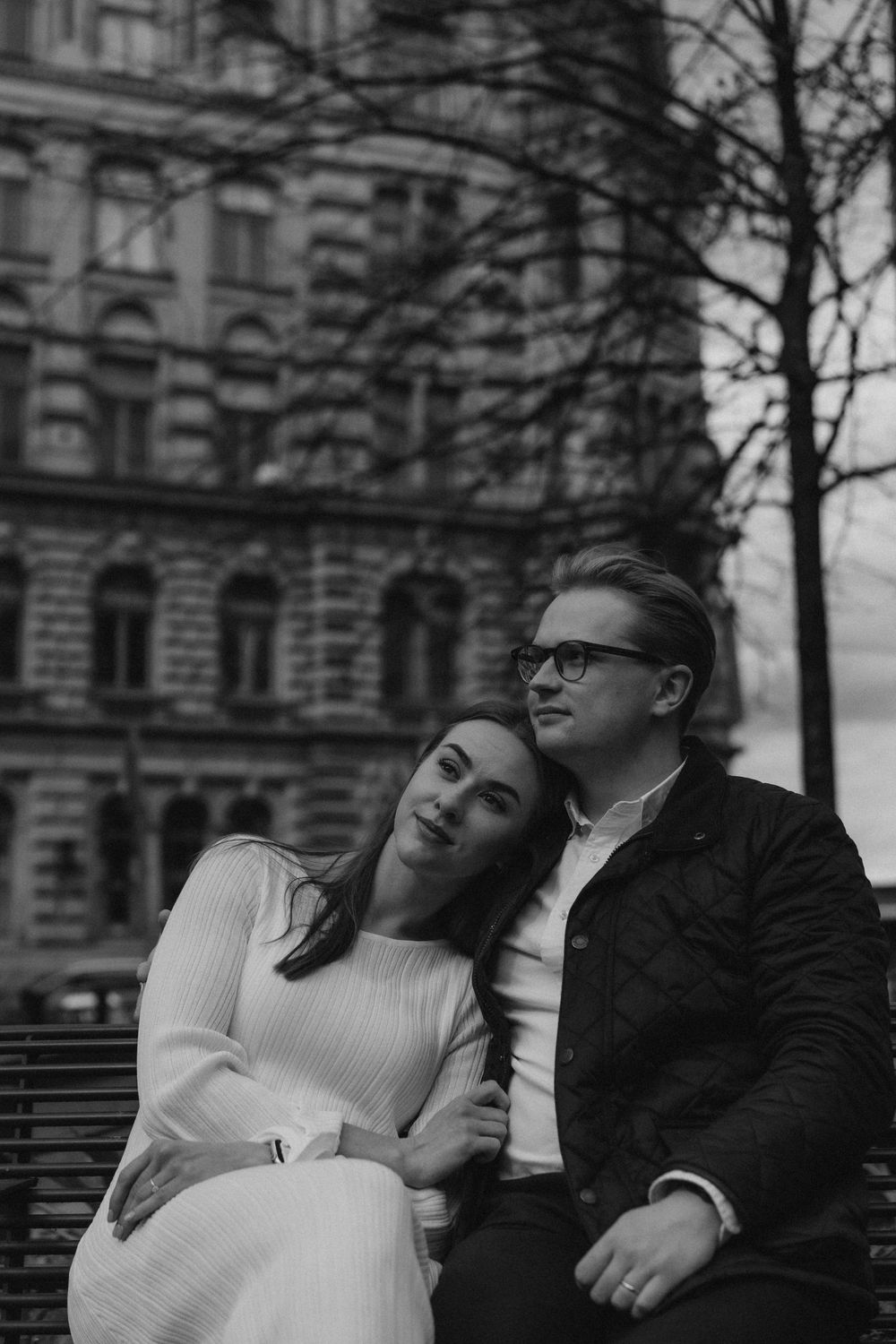 Black and white engagement photo of a couple sitting together in Helsinki city centre during a relaxed urban session