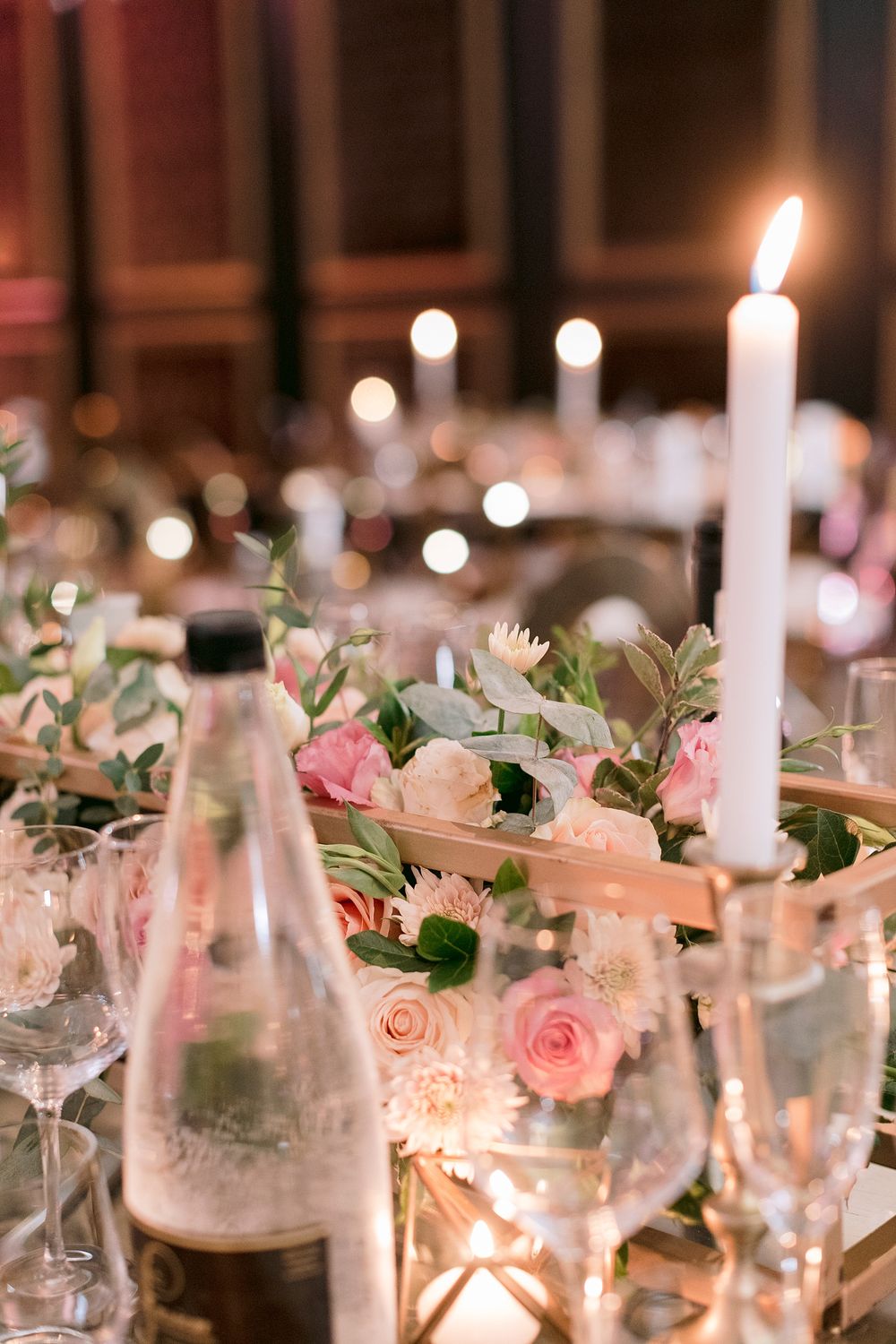 Wedding table detail featuring pink and white rose centerpiece, tall white taper candle, and crystal wine glasses.