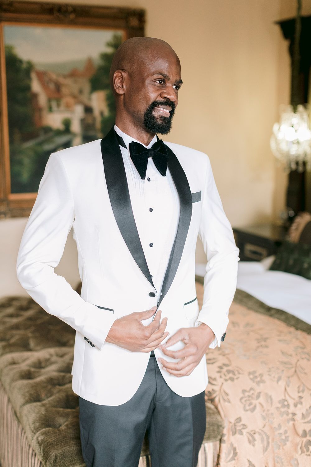 Handsome groom in white tuxedo jacket with black satin lapels and bow tie preparing for wedding.