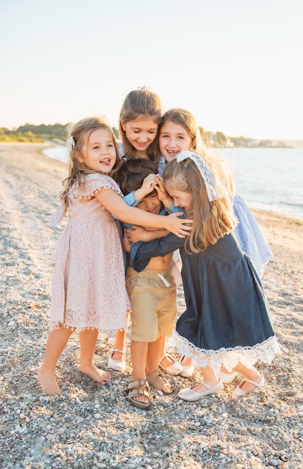 Five children hugging and laughing together on a sunny beach, dressed in pastel and navy outfits. extended family photoshoot Portsmouth RI