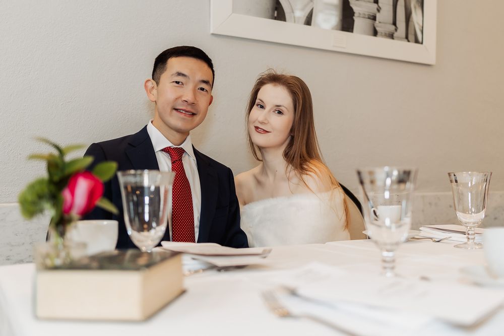 Couple in wedding attire seated at elegant reception table with glassware and floral centerpiece.