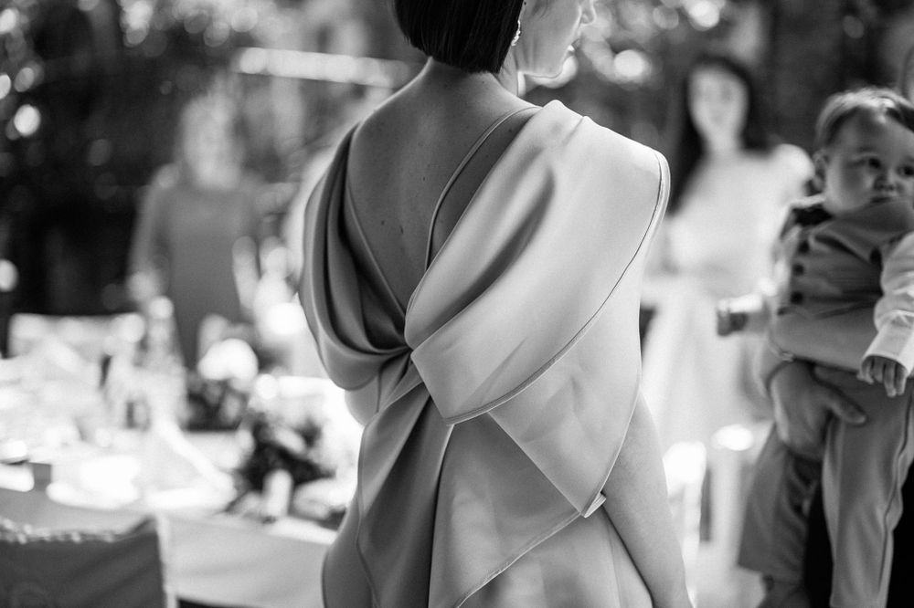 Elegant black and white photo showing back of dress with dramatic bow detail at outdoor event.