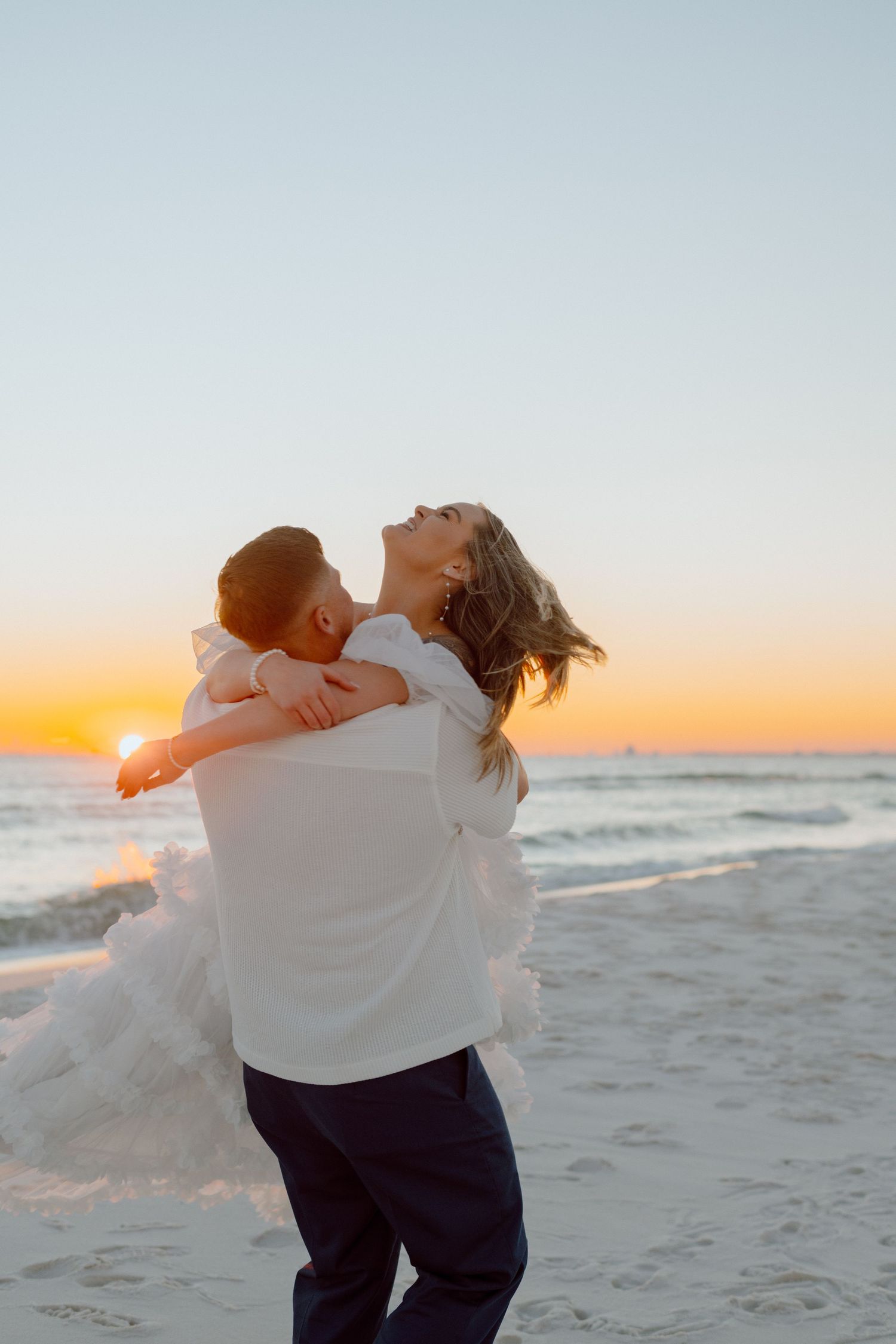 Romantic sunset embrace on a sandy beach with warm golden light glowing on the horizon and waves in the background.
