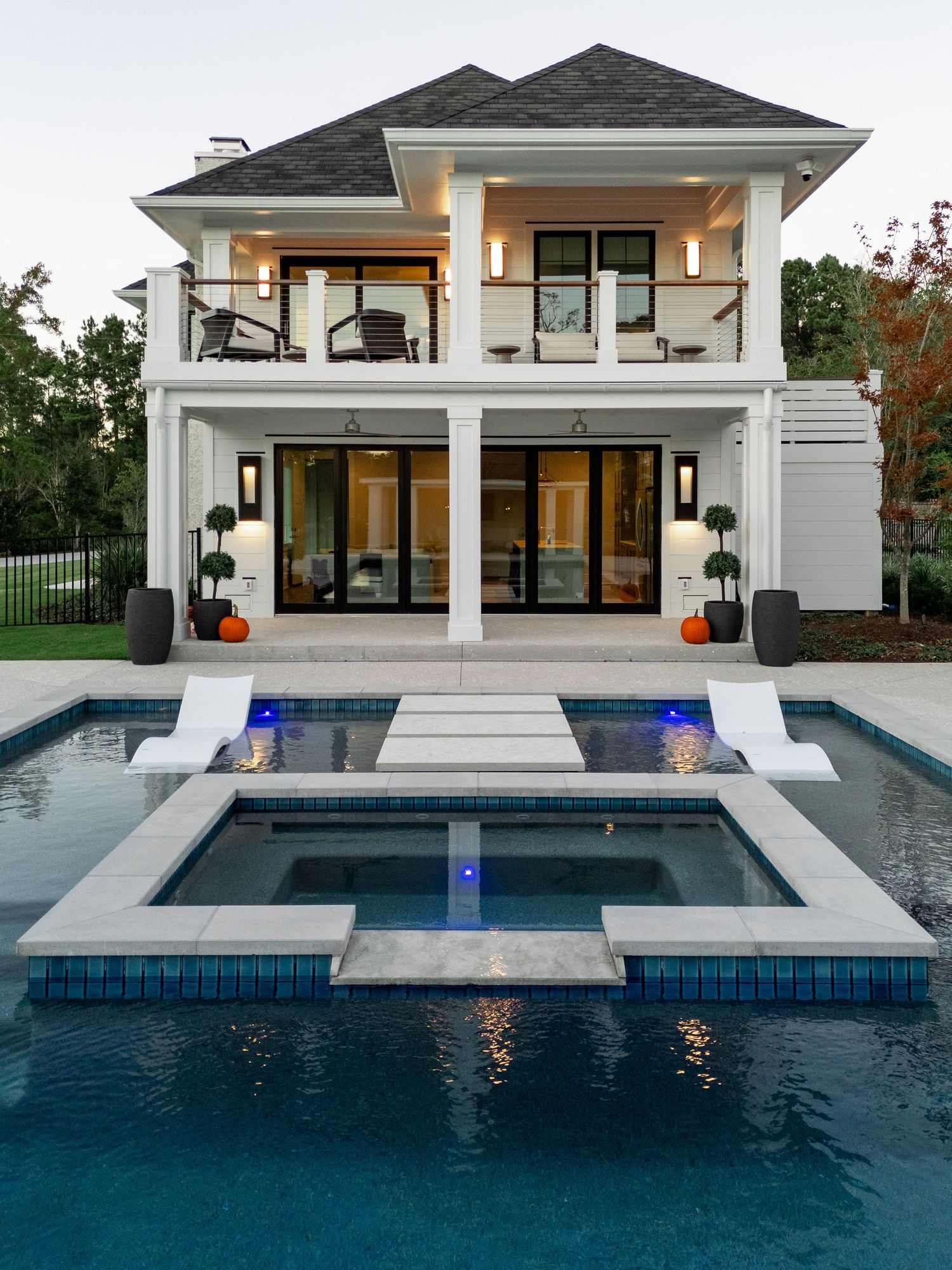 Modern white two-story house with pool and spa featuring dramatic lighting.