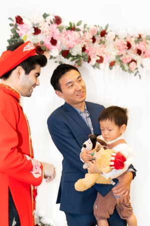 Family shares a heartwarming moment with a character and stuffed toy under a floral arch display at an event.