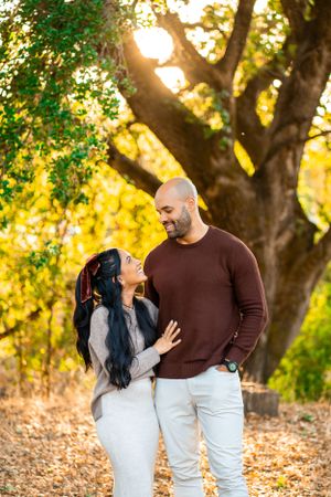 A loving couple shares a tender moment together under a golden sunlit tree during an autumn afternoon photoshoot.