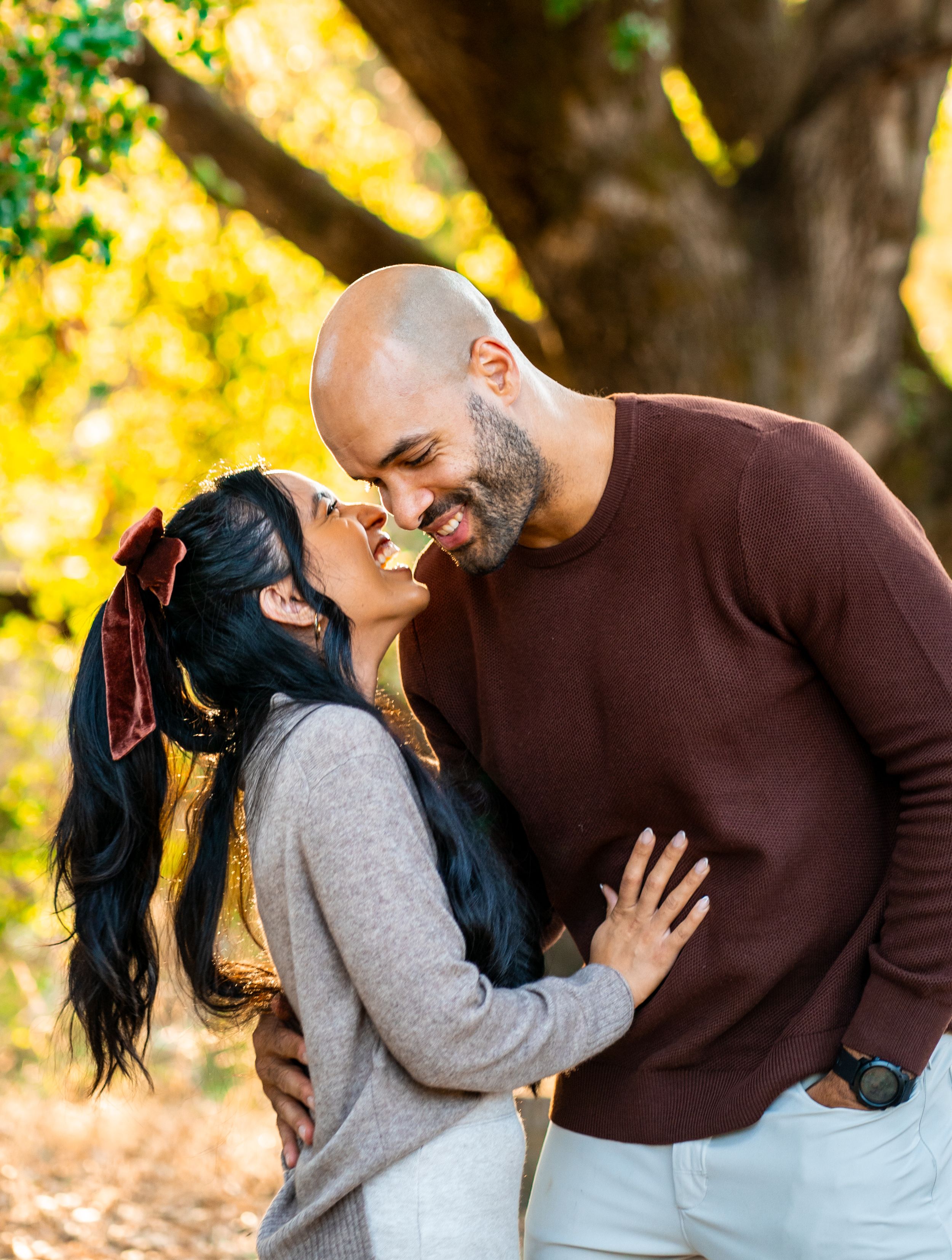 A couple shares a tender moment outdoors with autumn foliage in the background during a romantic photo session.
