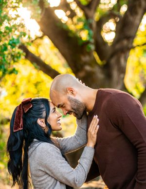 A couple sharing an intimate moment in a sunlit park with golden bokeh and autumn trees in the background.