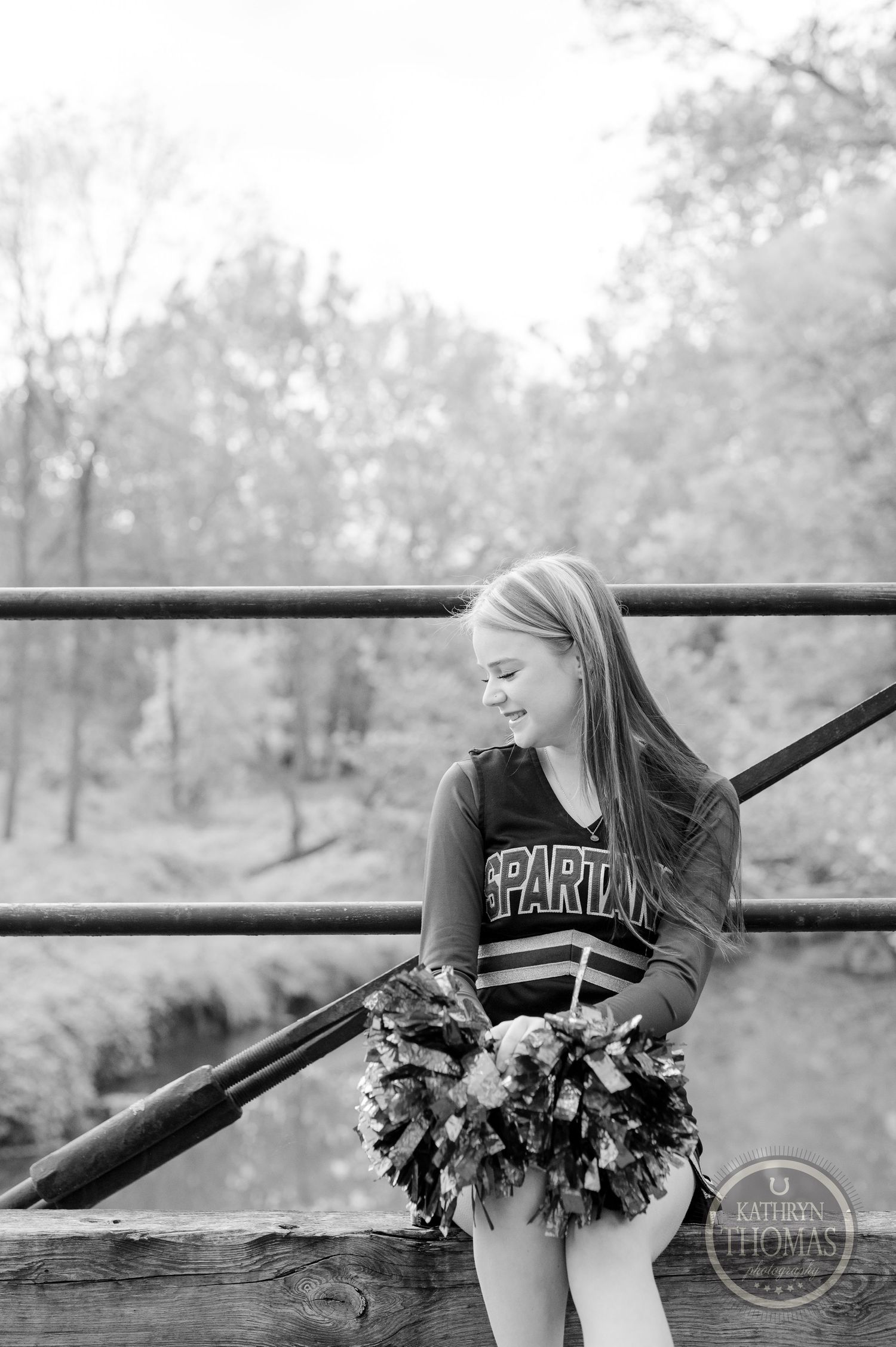 Cheerleader wearing a school uniform strikes a thoughtful pose on a wooden bridge in a black and white photo.